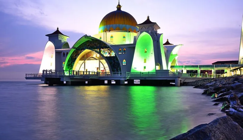 Melaka Straits Mosque in Malacca, Malaysia beautifully lit at sunset over the water.