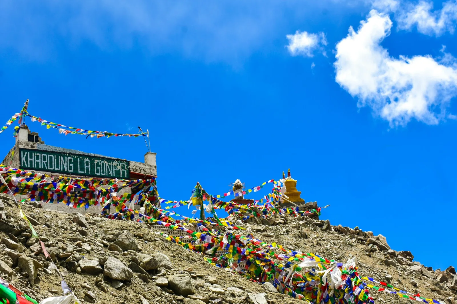 Colorful prayer flags at Khardung La Pass in Ladakh under a clear blue sky.