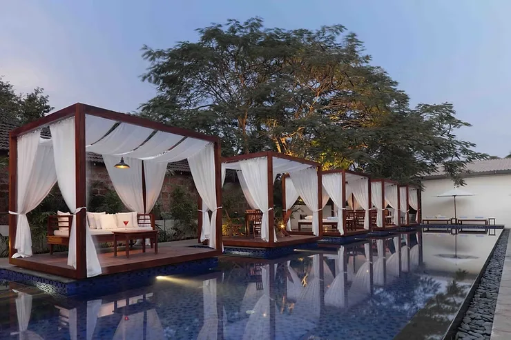 Romantic canopy seating beside a serene swimming pool at a high-end Goa hotel.