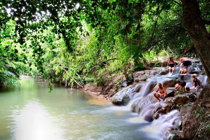 People relaxing in a natural hot spring waterfall surrounded by lush green jungle.