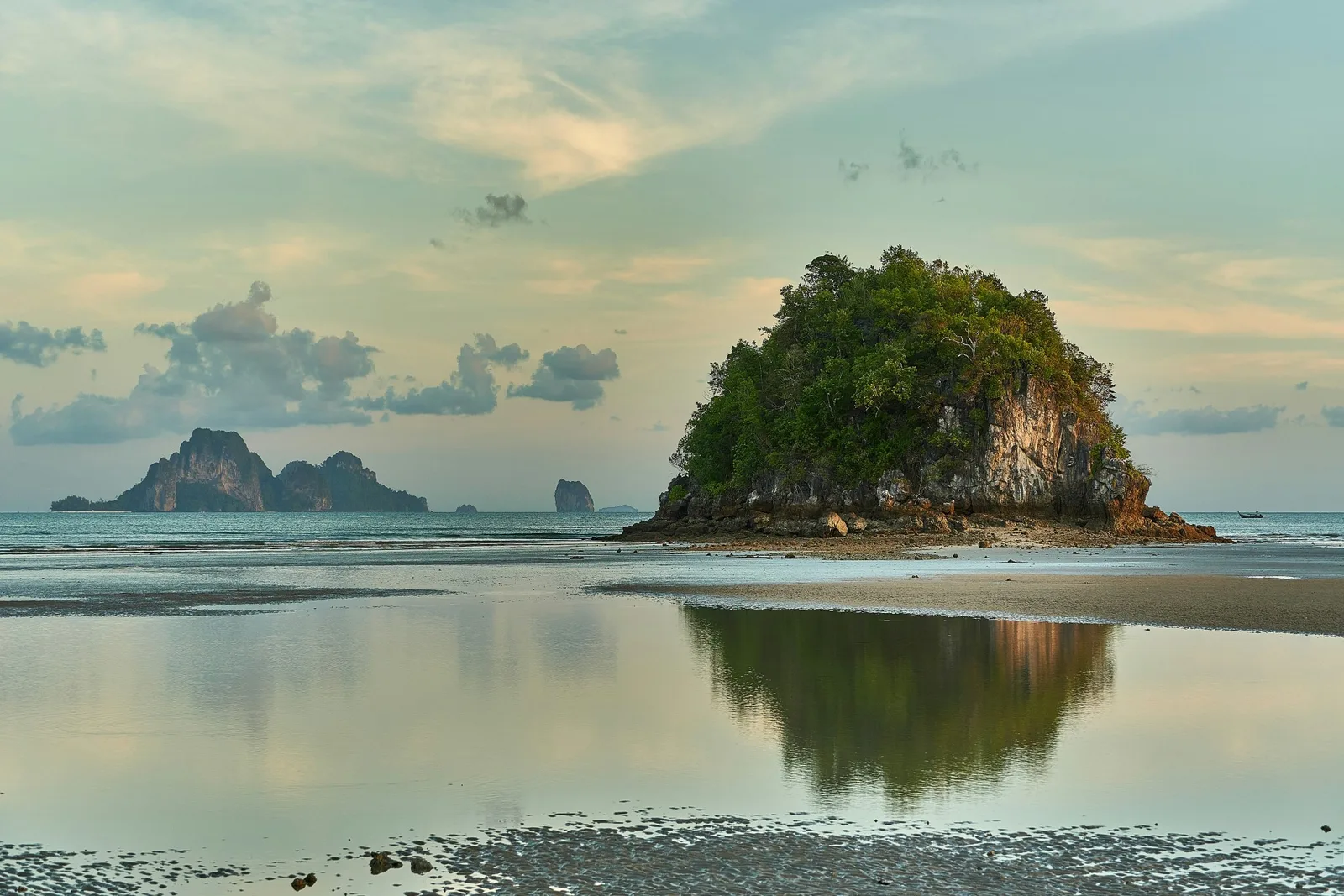 Scenic view of Ao Nang, Thailand with calm sea, island cliffs, and sunset reflection.