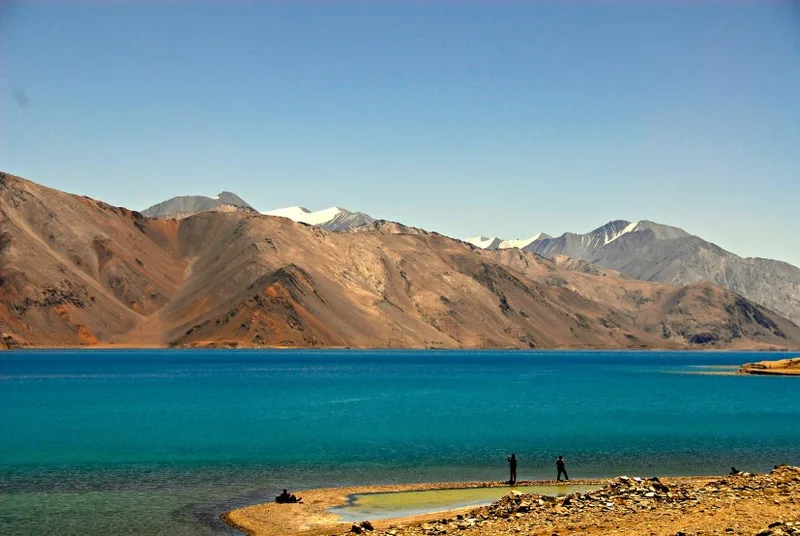 Snow-capped mountains with a clear blue river flowing through a rugged valley in Ladakh.