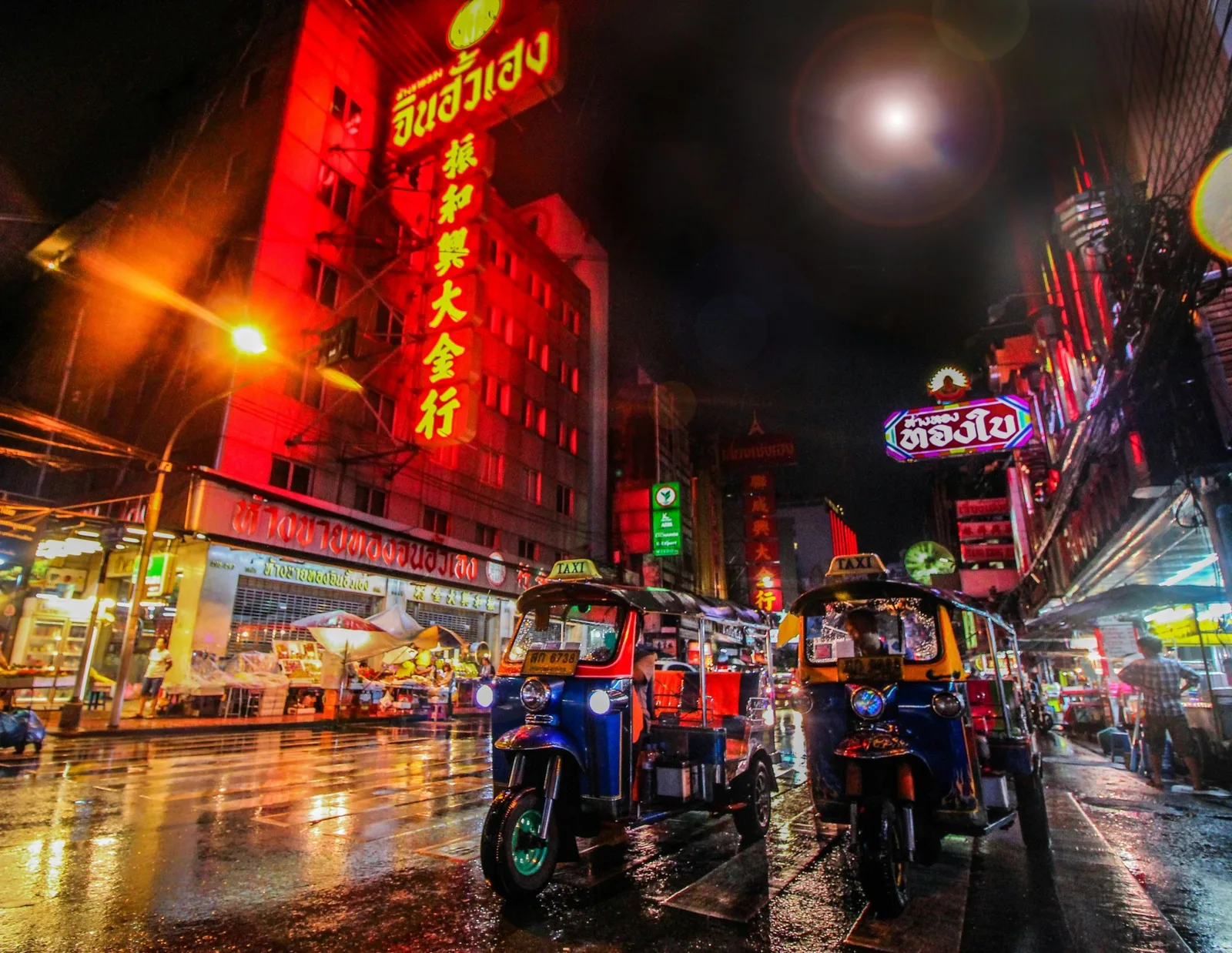 Bangkok Chinatown at night with tuk-tuks and neon lights on a rainy street.