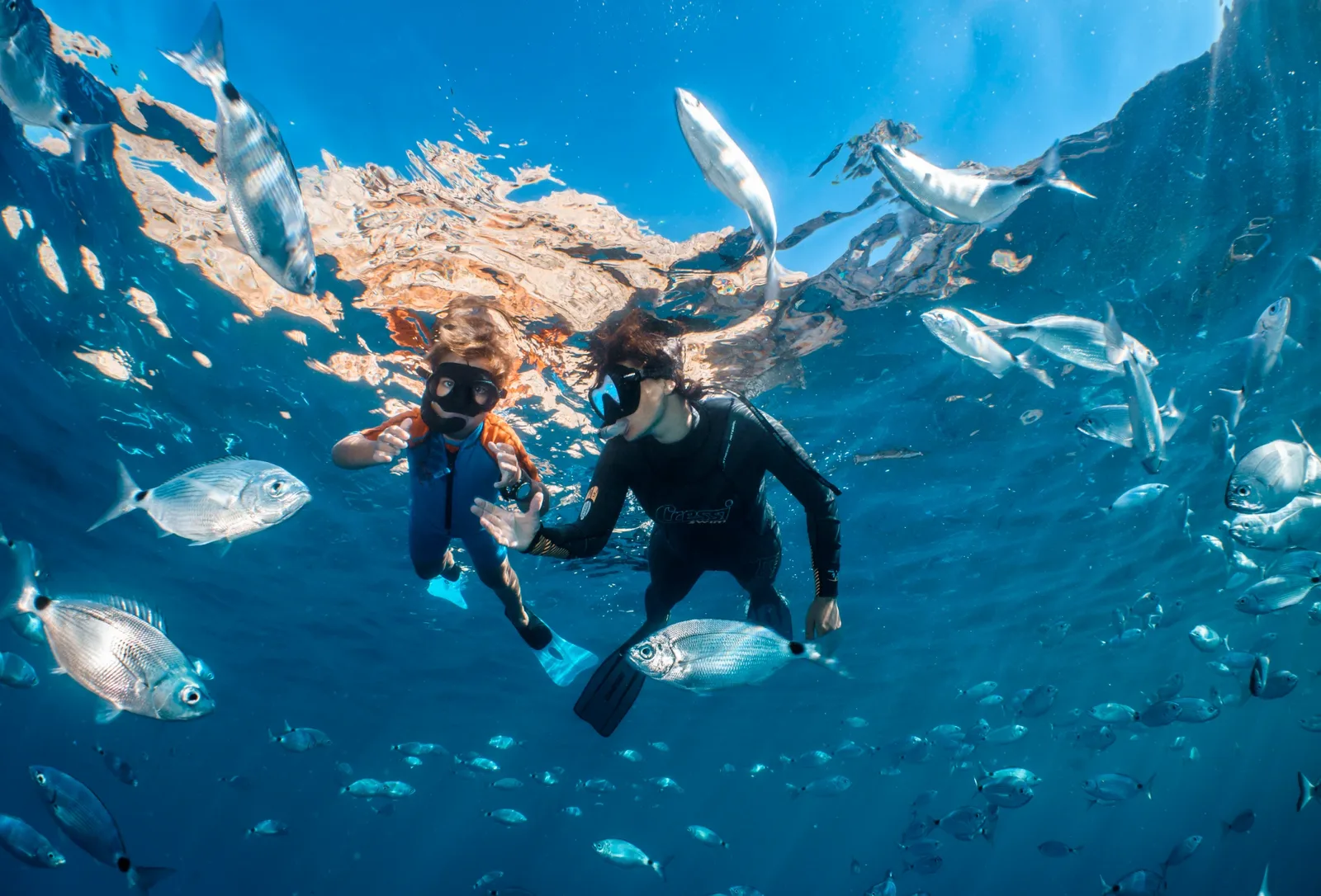 A mother and her child scuba diving in the stunning waters of Costa Brava, exploring the vibrant marine life.